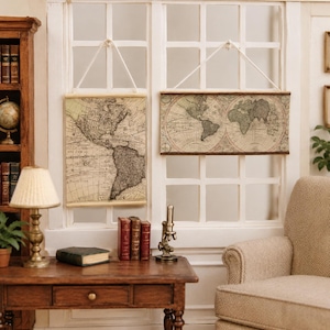 May include: Two miniature wall hangings featuring vintage-style world maps printed on paper. One map is oriented vertically showing the Americas, while the other is horizontal showing the globe. Both are suspended by white string from wooden rods.