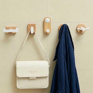 May include: A collection of wooden wall hooks with white accents. A white purse hangs from one hook, and a blue towel hangs from another. The hooks are mounted on a light beige tiled wall, offering a minimalist and functional design.