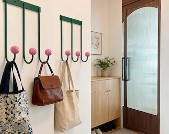 Puede incluir: Dos percheros de pared de metal verde con extremos de bola rosa, que sostienen bolsas de varios estilos y colores. Los ganchos están montados en una pared blanca. Un bolso de cuero marrón y una bolsa de lona cuelgan de los ganchos.