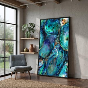 May include: Large framed art print featuring an abstract design of iridescent blue and green abalone shells. The artwork has a black frame and is leaning against a neutral-colored wall. The print's colors include teal, turquoise, and hints of orange.