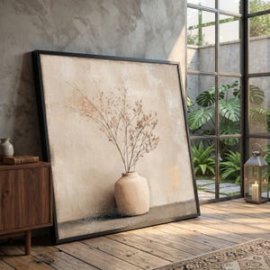 Könnte beinhalten: Ein großer, gerahmter Leinwandkunstdruck mit einer beigefarbenen Vase mit getrockneten Blumenstielen. Das Kunstwerk hat eine neutrale Farbpalette mit strukturiertem Hintergrund. Der schwarze Rahmen lehnt an einer Wand in einem Raum mit einem Fenster.
