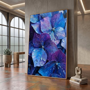 May include: A framed canvas print depicting a close-up of blue and purple hydrangea flowers. The artwork shows detailed brushstrokes and water droplets, creating a realistic texture. The floral art is set in a room with natural light.