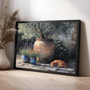 May include: Framed art print depicting a serene outdoor scene. A large, weathered terracotta pot holds a small olive tree. Two blue pots with flowers sit in front. An orange cat sleeps on the stone ground. The artwork is framed in black.