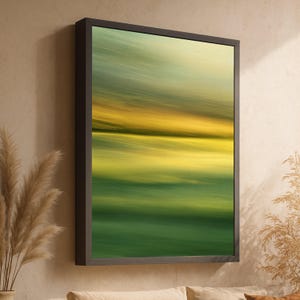 Puede incluir: Impresión artística abstracta en un marco oscuro. La obra presenta un paisaje borroso con tonos de verde, amarillo y azul, creando una sensación de movimiento y profundidad. El arte enmarcado está montado en una pared de color neutro.