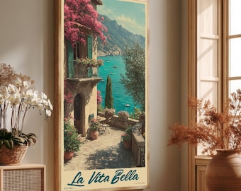 May include: A vertical wall art print featuring a coastal Mediterranean scene with a stone building adorned with pink flowers, a balcony, and a terrace overlooking a turquoise sea and mountains. The text La Vita Bella is printed at the bottom.