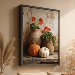 May include: A framed still life painting featuring two pumpkins, one orange and one white, next to two terracotta pots with red geraniums. The background is a textured stone wall, and the frame is dark.