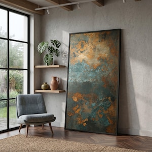 May include: A large framed abstract art piece with a black frame. The artwork features a blend of teal, copper, and brown hues, creating a textured, weathered appearance. A gray armchair, wooden shelves with vases, and a large window are also visible.