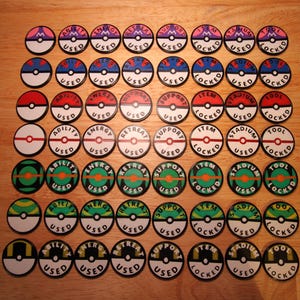 May include: A collection of circular game tokens with various designs and text. The tokens feature red, white, blue, green, and yellow color schemes. Text includes "USED", "ABILITY", "ENERGY", "RETREAT", "SUPPORT", "ITEM", "STADIUM", and "TOOL".