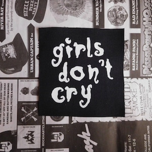 May include: Black and white iron-on patch with the text "girls don't cry" in white lettering on a black background.