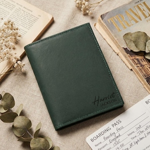 May include: A dark green leather passport holder with the name "Harriet Jackson" in cursive script. The passport holder is next to a vintage travel magazine and a boarding pass.