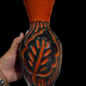 May include: A ceramic vase with a flared orange rim and a dark blue body. The vase features an orange leaf design with green accents. The vase is approximately 10 inches tall.