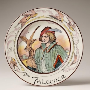 Può includere: Un piatto rotondo in ceramica con un'illustrazione centrale di una persona con cappello rosso e mantello verde che tiene un falco su una mano guantata. Il bordo mostra uccelli in volo e nuvole, con il testo The Falconer stampato in basso.