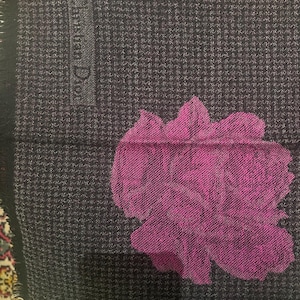May include: A dark gray scarf with a small houndstooth pattern and a large magenta floral design. The scarf has a fringed edge and the text "Christian Dior" is visible.