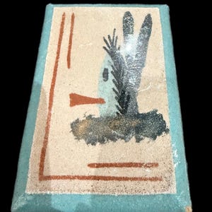 Op de afbeelding: Rechthoekig kunstwerk met een lichtbeige achtergrond, een turquoise rand en abstracte beelden. Het kunstwerk toont een zwart-grijze plantachtige vorm, een rood-oranje vorm en rood-oranje lijnen. Het stuk is waarschijnlijk een schilderij of een print.