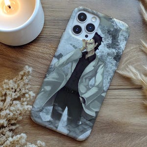 May include: A phone case featuring an anime-style illustration of a man in a white coat and black attire. The case has a gray and white background with a textured appearance. The phone case is on a wooden surface.