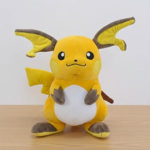May include: A plush yellow Raichu toy with brown-tipped ears, feet, and tail. The toy has a white belly, black eyes, and a small, smiling mouth. The Raichu plush is a popular character from the Pokémon franchise.
