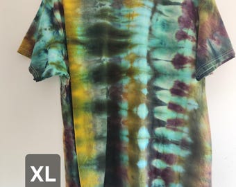 Può includere: Una t-shirt a maniche corte con girocollo caratterizzata da un motivo tie-dye nei toni del giallo senape, verde ottanio, verde scuro e viola intenso. La maglia presenta un effetto a righe verticali creato dalla tintura e un'etichetta taglia XL.