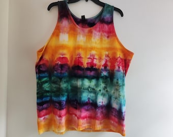 Può includere: Una canotta senza maniche caratterizzata da un vivace motivo tie-dye con bande orizzontali di colore giallo, arancione, rosso, viola, blu e verde. Il capo presenta uno scollo rotondo ed è esposto su una gruccia nera su sfondo bianco.