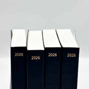 May include: Four dark blue hardcover books with white pages. The year "2026" is printed in gold on the spine of each book. The books are stacked together against a white background.