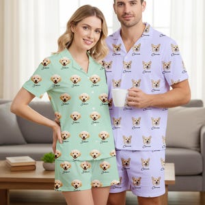 May include: Matching pajama sets featuring a dog face pattern. One set is light green with a golden retriever design and the name "John". The other set is lavender with a corgi design and the name "Claire".