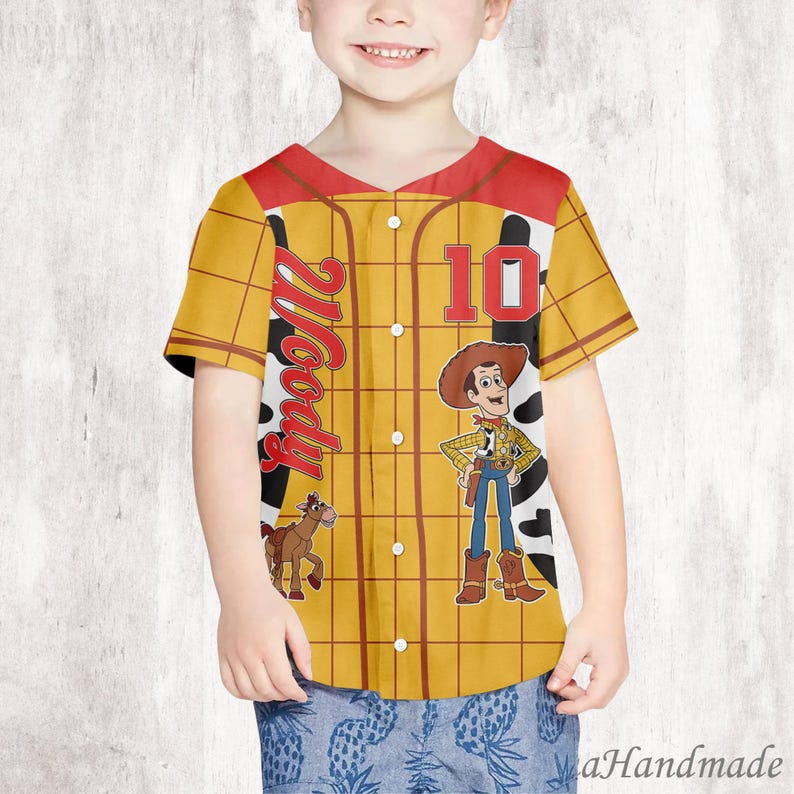 May include: A yellow baseball jersey with a red collar and sleeves, featuring the character Woody from Toy Story. The jersey has the number 10 and the name "Woody" printed on it, along with an image of Woody and a horse.