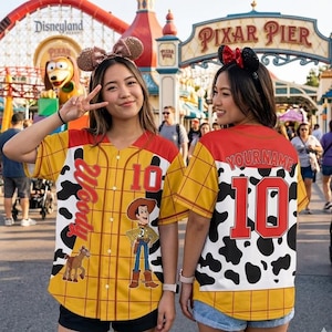 May include: Two yellow baseball jerseys with red and white accents, featuring a Woody design. One jersey has the number 10 and the name "Woody" on the front. The other jersey has the number 10 and the text "YOURNAME" on the back. Both jerseys are worn at Disneyland.