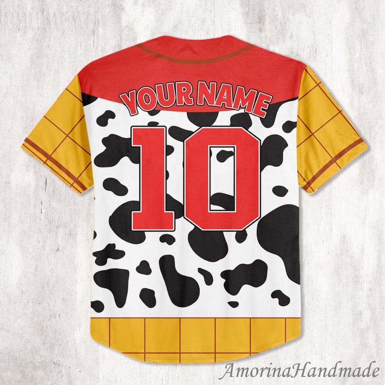 May include: A short-sleeved baseball jersey with a red yoke and collar, featuring the text "YOUR NAME" above a large red number "10". The jersey has a white base with black cow spots, yellow sleeves, and a yellow hem.