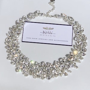 May include: A silver necklace with a delicate chain and a large cluster of clear crystals in a leaf-like design. The necklace is displayed on a white background with a business card that reads "Salvatore Design Fine Hair Jewelry and Accessories".