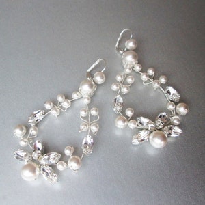 May include: A pair of silver earrings with a delicate design featuring white pearls and clear crystals. The earrings are shaped like a teardrop and dangle from the ear.