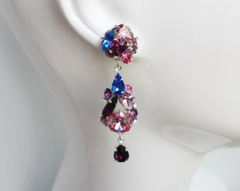May include: A pair of dangle earrings with a cluster of pink, purple, and blue crystals. The earrings are silver-toned and have a teardrop shape.