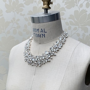 May include: A white dress form with a silver rhinestone necklace. The dress form is on a white background with a floral pattern.