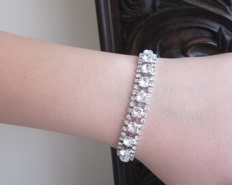 May include: A silver bracelet with a row of clear rhinestones. The bracelet is on a person's wrist.
