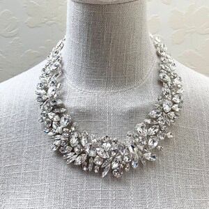 May include: A silver statement necklace with large, clear crystal stones arranged in a floral pattern.