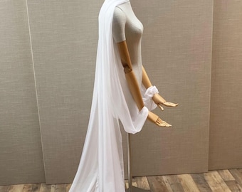 May include: A white sheer fabric draped over a mannequin. The fabric is long and flowing, with a train that trails behind the mannequin.