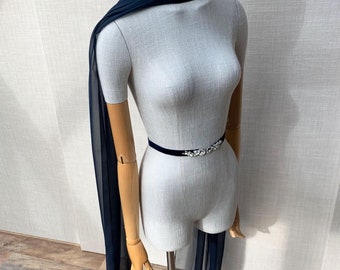 May include: A navy blue sheer scarf draped over a mannequin's shoulders. The scarf is long and flowing, with a delicate texture. A black velvet belt with a rhinestone embellishment is worn around the mannequin's waist.
