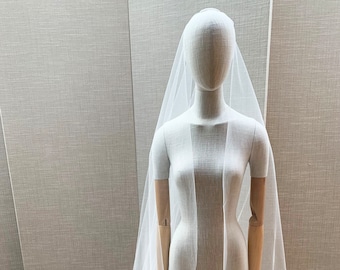 May include: A white tulle wedding veil with a long, flowing train. The veil is draped over a mannequin and is displayed on a silver stand.