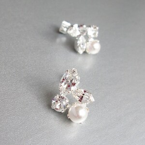 May include: A pair of silver earrings featuring a cluster of clear rhinestones and a single pearl at the centre of each earring.