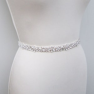 May include: A white satin bridal sash with a delicate row of clear crystal embellishments.