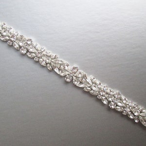 May include: A silver rhinestone trim with a floral design. The trim is made of small, clear rhinestones that are arranged in a delicate pattern.