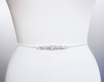 May include: A silver chain belt with a crystal embellishment. The belt is on a white dress form.