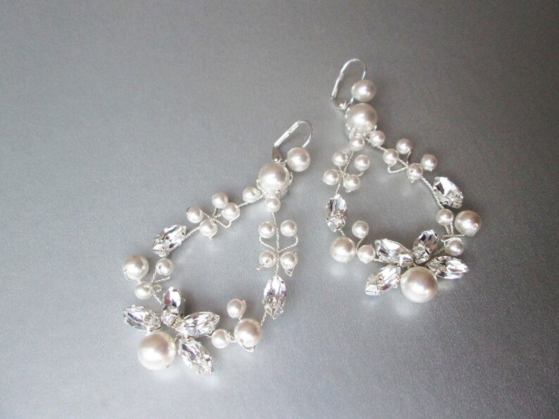 May include: A pair of silver earrings with a delicate design featuring white pearls and clear crystals. The earrings are shaped like a teardrop and dangle from the ear.