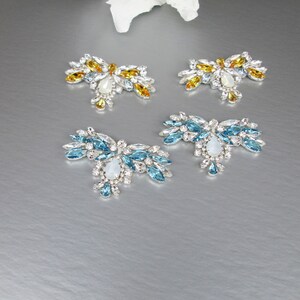 May include: Four decorative embellishments with crystal-like stones. Two are blue and two are yellow.