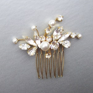 Puede incluir: Un peine de pelo dorado con un grupo de piedras de cristal transparentes y perlas blancas. El peine tiene un dise&ntilde;o floral delicado.
