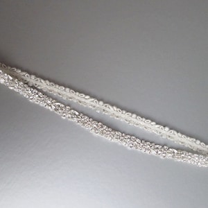 May include: A white satin bridal sash with a beaded design featuring clear rhinestones.