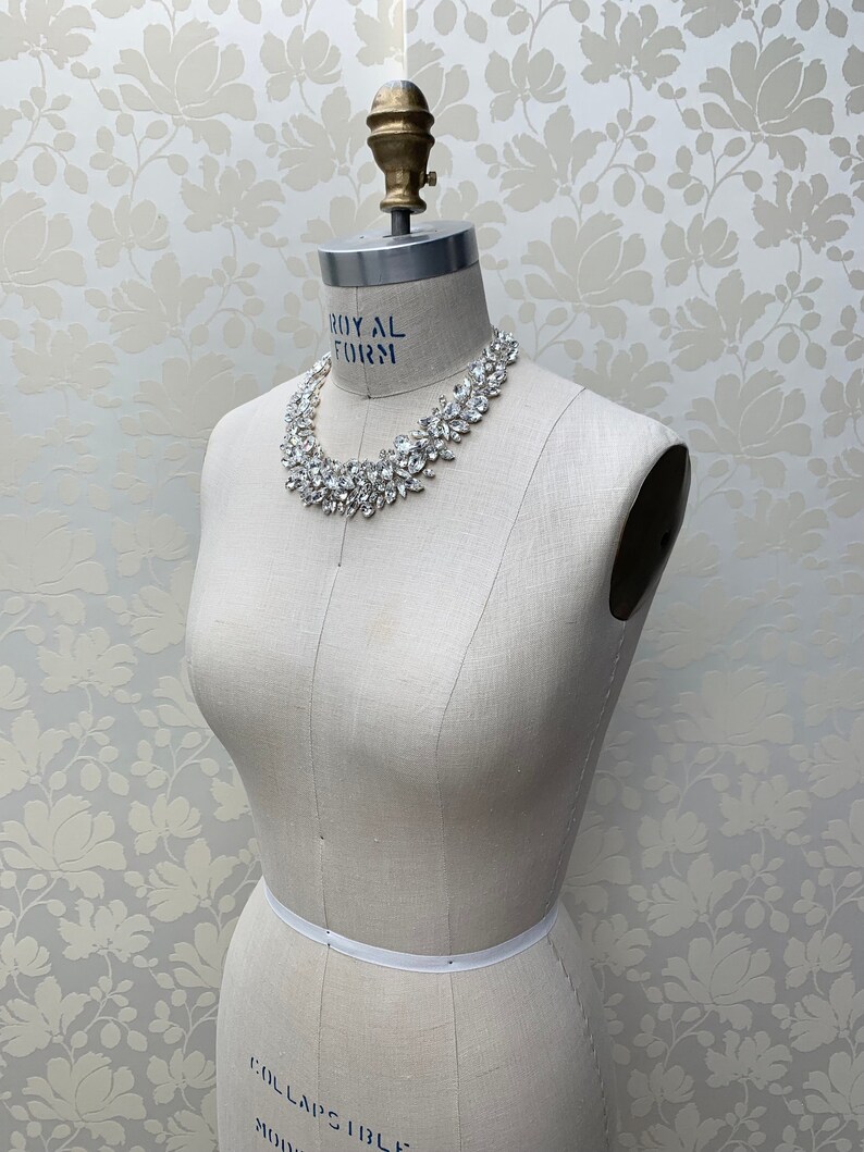 May include: A white dress form with a silver rhinestone necklace. The dress form is on a white background with a floral pattern.