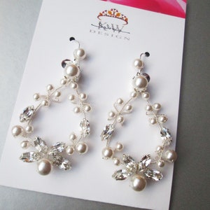 May include: A pair of silver earrings with a delicate floral design featuring small white pearls and clear crystals. The earrings are displayed on a white card with the text "KW DESIGN" printed on it.