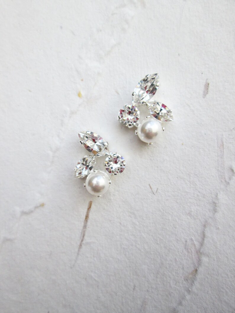 May include: A pair of silver earrings with a pearl and crystal accents. The earrings are small and delicate.