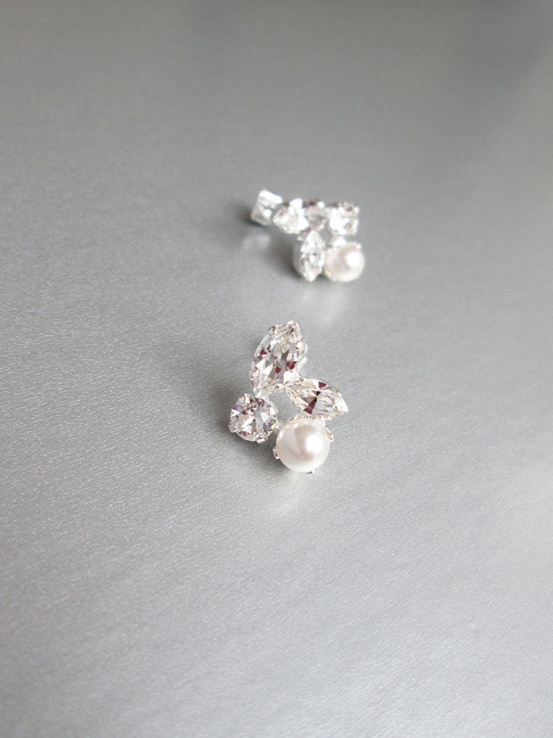 May include: A pair of silver earrings featuring a cluster of clear rhinestones and a single pearl at the centre of each earring.