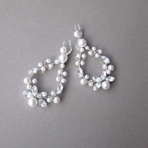 May include: A pair of silver earrings with a delicate design featuring white pearls and clear crystals. The earrings are shaped like a teardrop with a floral motif.