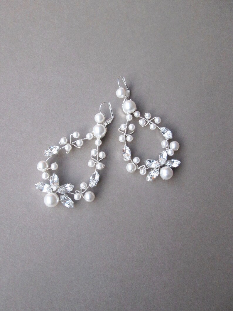 May include: A pair of silver earrings with a delicate design featuring white pearls and clear crystals. The earrings are shaped like a teardrop with a floral motif.